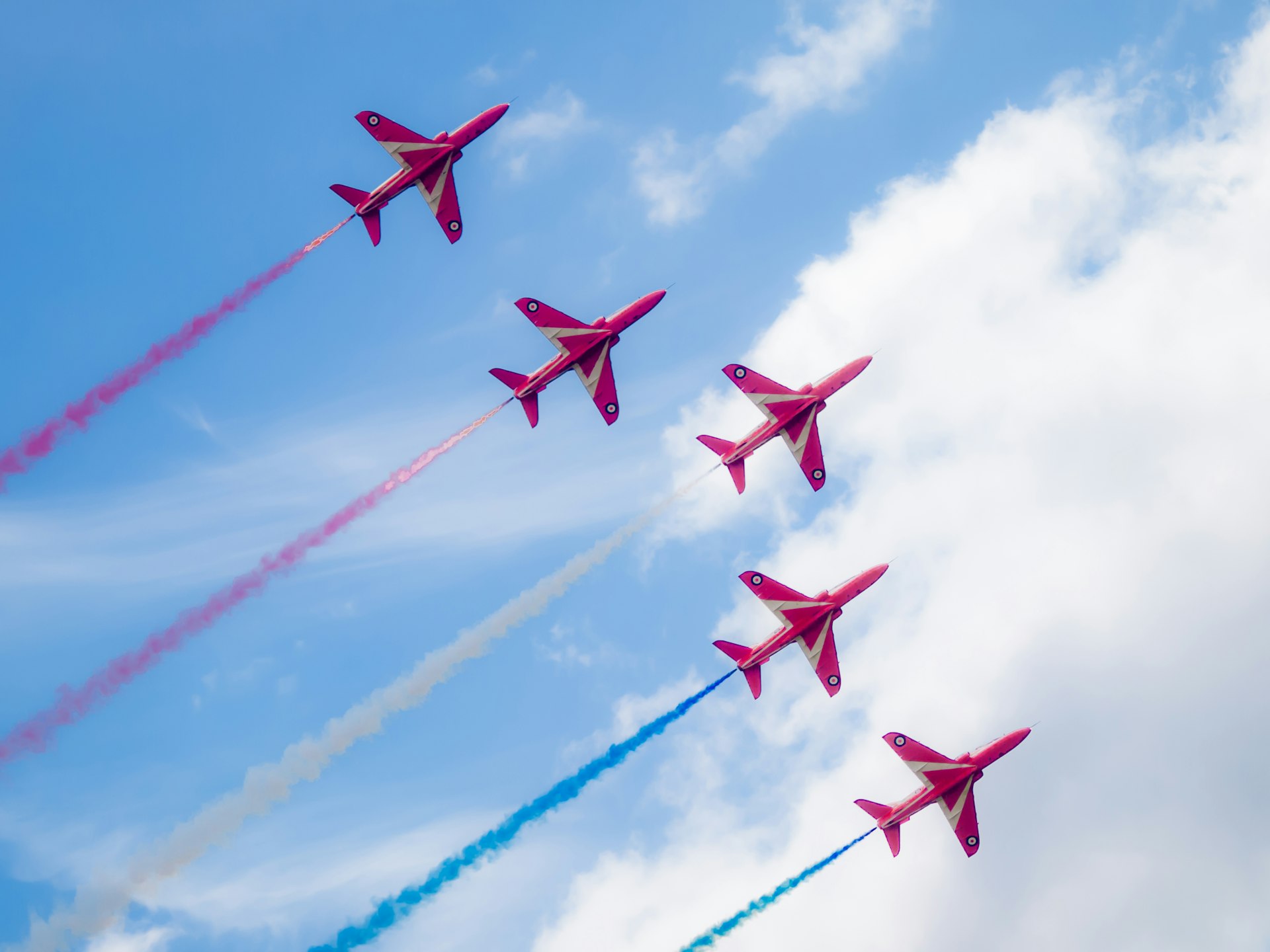 a group of jets flying through a blue cloudy sky